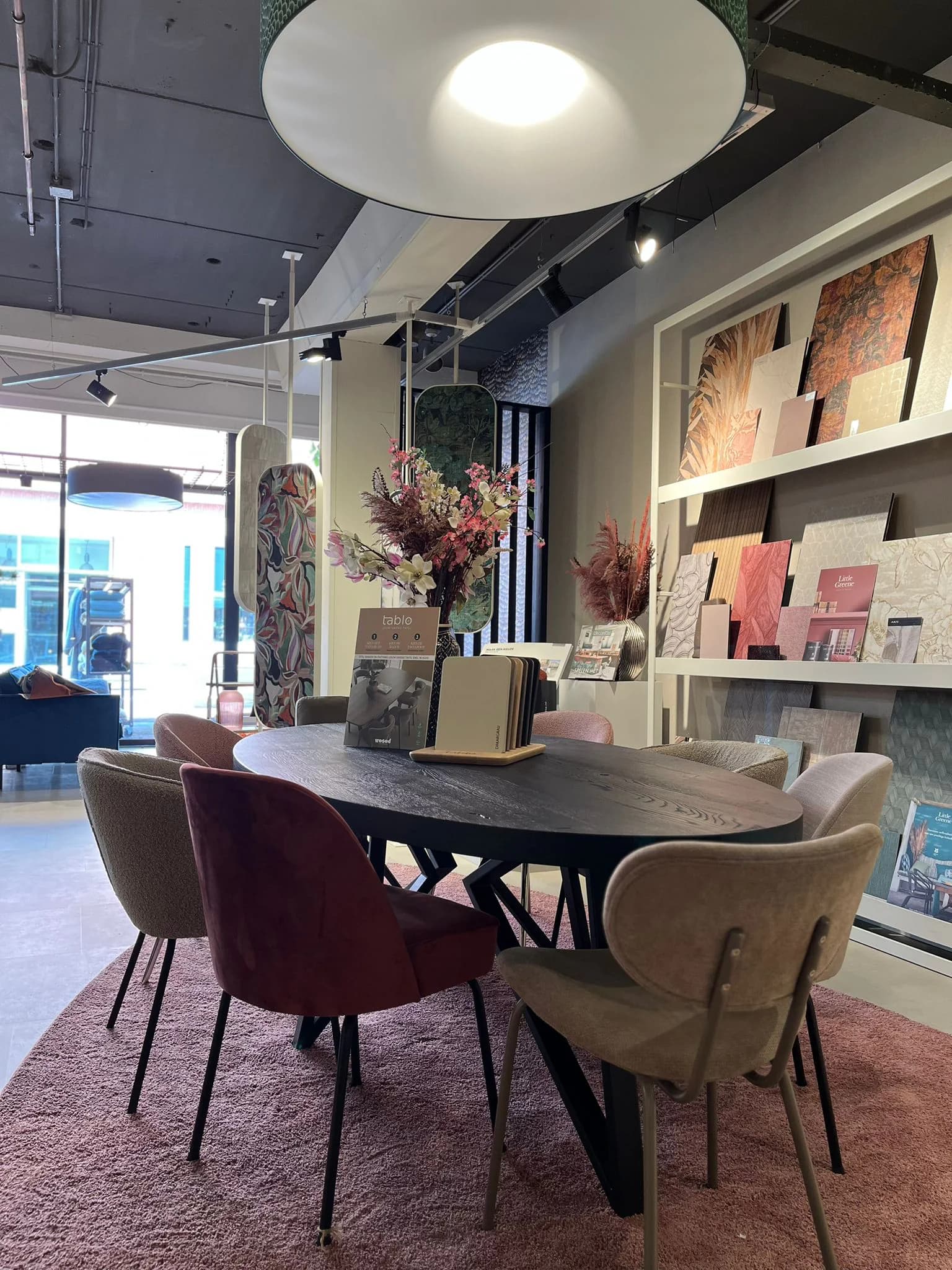 Ronde ontwerptafel met stoelen voor een wand vol behangstalen