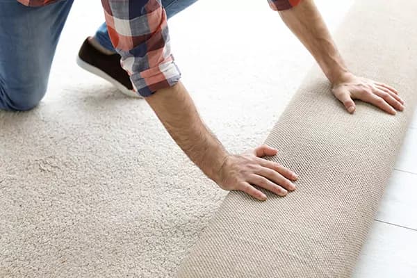 Stoffeerder rolt beige kamerbreed tapijt uit