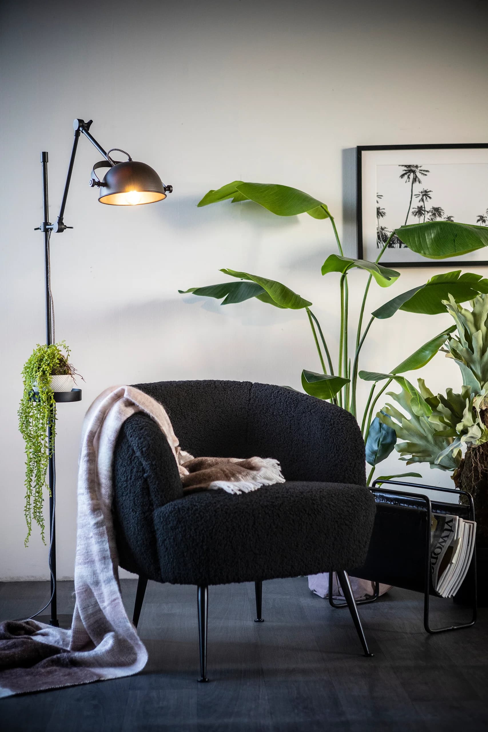 Zwarte bouclé fauteuil met plaid naast een vloerlamp