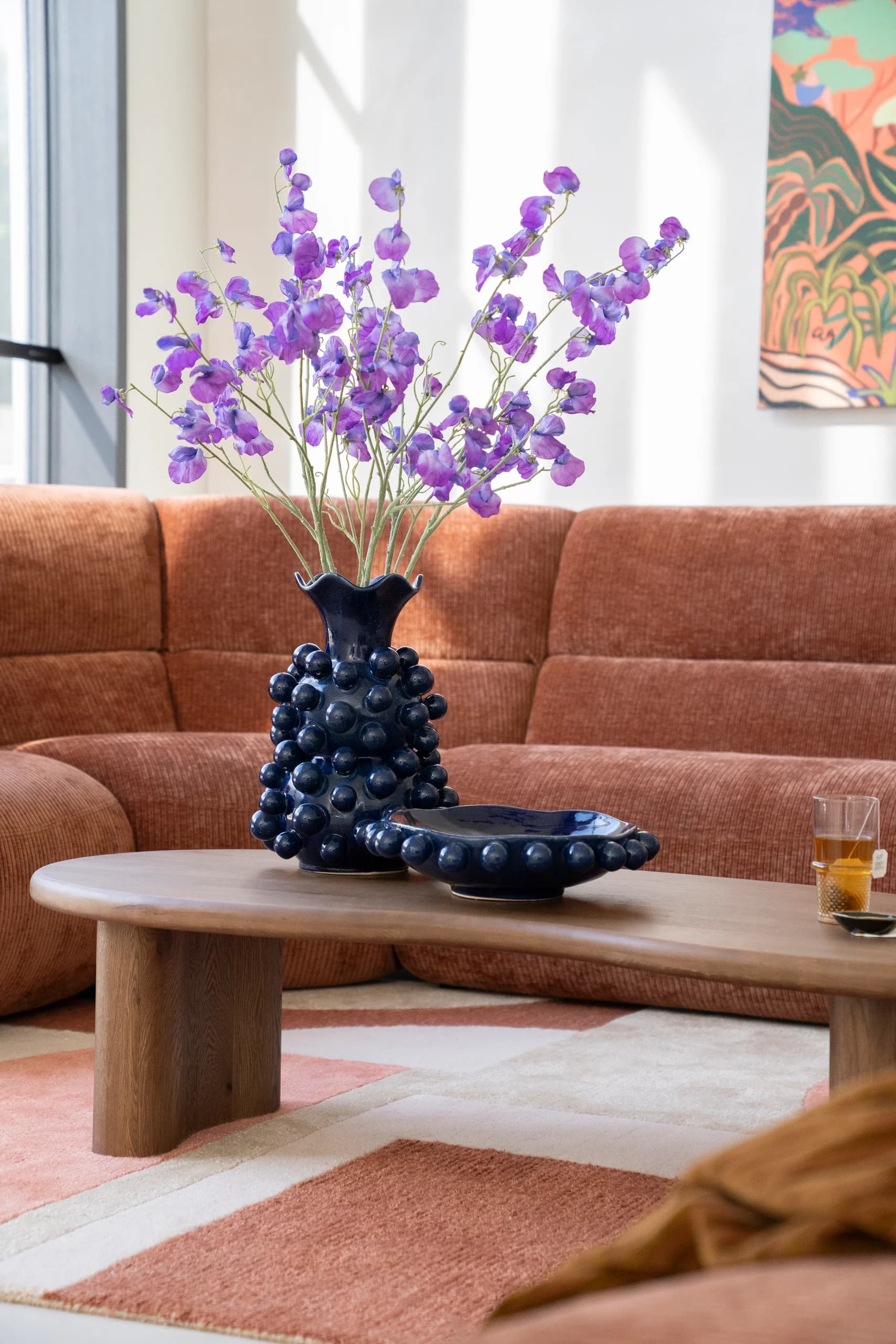 Lage houten salontafel met blauwe vaas voor een terracotta bank