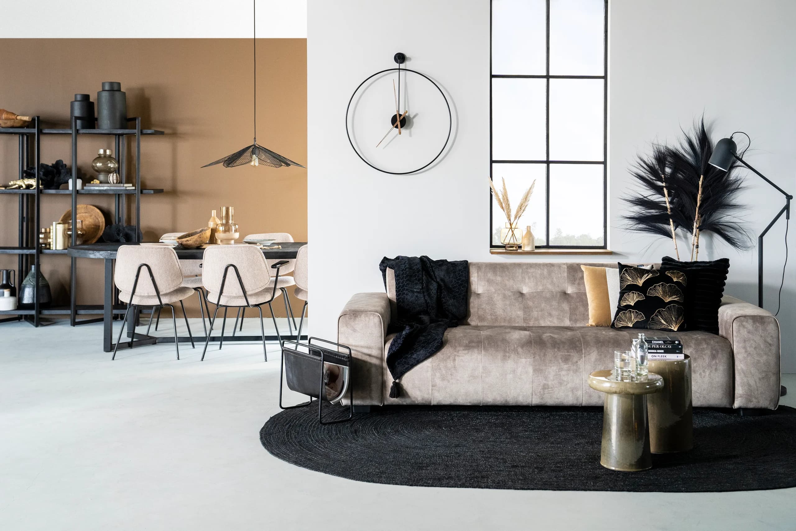 Lichte loftwoonkamer met beige bank, ronde poef en een eethoek met zwarte stoelen