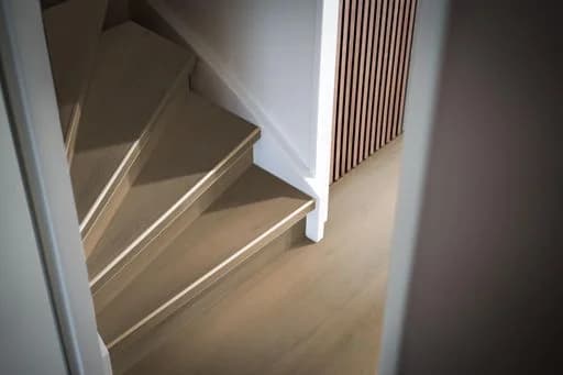 Gerenoveerde trap met treden in houtlook van Ambiant en witte stootborden