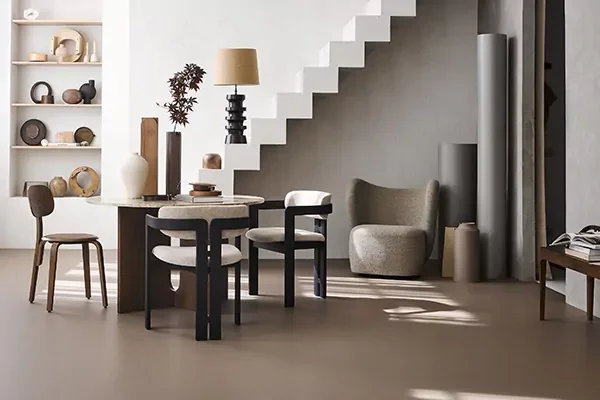 Lichte ruimte met een witte trap, een fauteuil, een ronde eettafel en een taupe marmoleumvloer