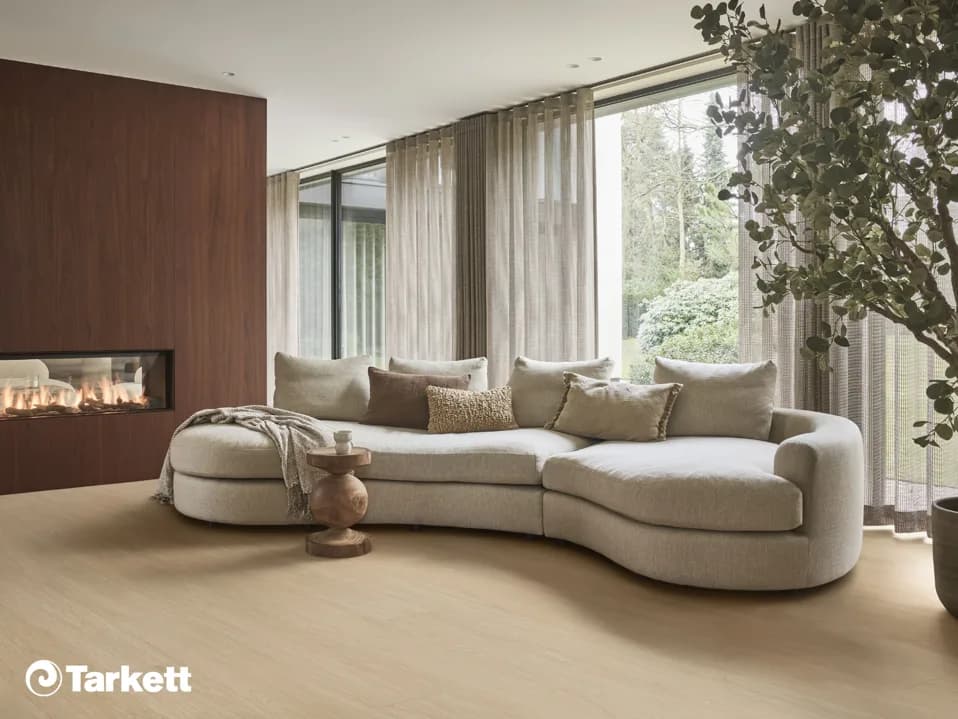 Woonkamer met een haard, een ronde bank en een lichte pvc-vloer van Tarkett in eikenlook