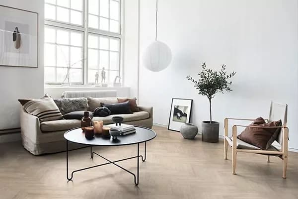 Lichte woonkamer met een olijfboom, een ronde salontafel, een linnen bank en een visgraat vinylvloer
